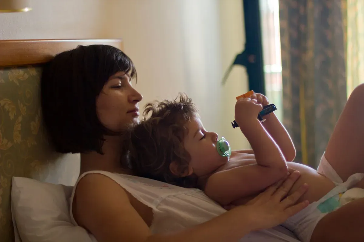 Eine erwachsene Person, die neben einem im Bett ruhenden Kleinkind liegt