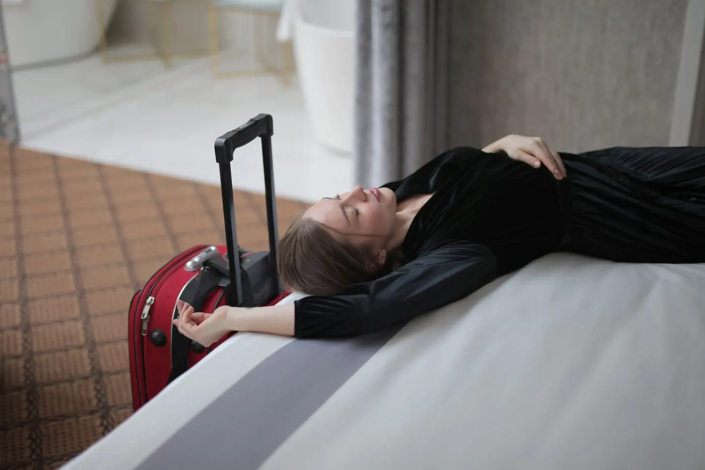 Eine erschöpfte Reisende ruht auf einem Hotelbett neben ihrem Koffer