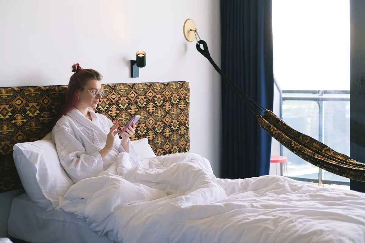Eine Reisende schaut vom Hotelbett aus auf ihr Telefon